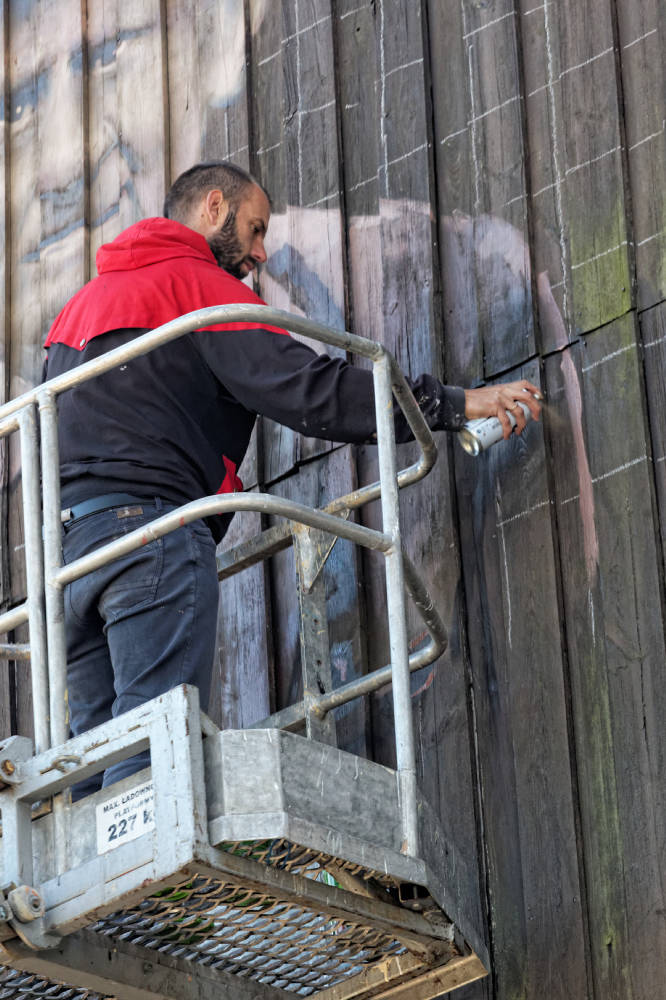Arkadiusz Andrejkow maluje drewnal na dworcu w Hajnówce